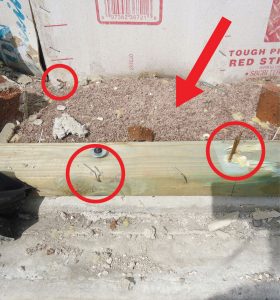 Figure 3. The flexible sheathing tore away from the bottom plate where staples were only partially embedded, allowing the balance of the wall to move inside (note that the arrow is pointing at the carpet).