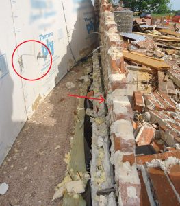 Figure 6. Damage consistent with previous tornado assessments – circle shows brick façade failure, arrow points to mortar buildup between bottom plate and brick veneer.