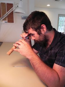 Examining the end grain of a timber specimen with a hand lens to identify the wood species.